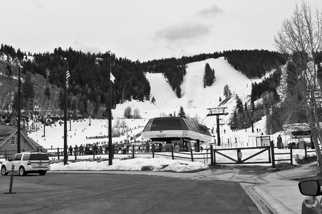 View of Deer Valley Resort’s base area featuring the Carpenter Express lift. Skiers gather near the lift with snow‑covered slopes and forested mountains rising behind.